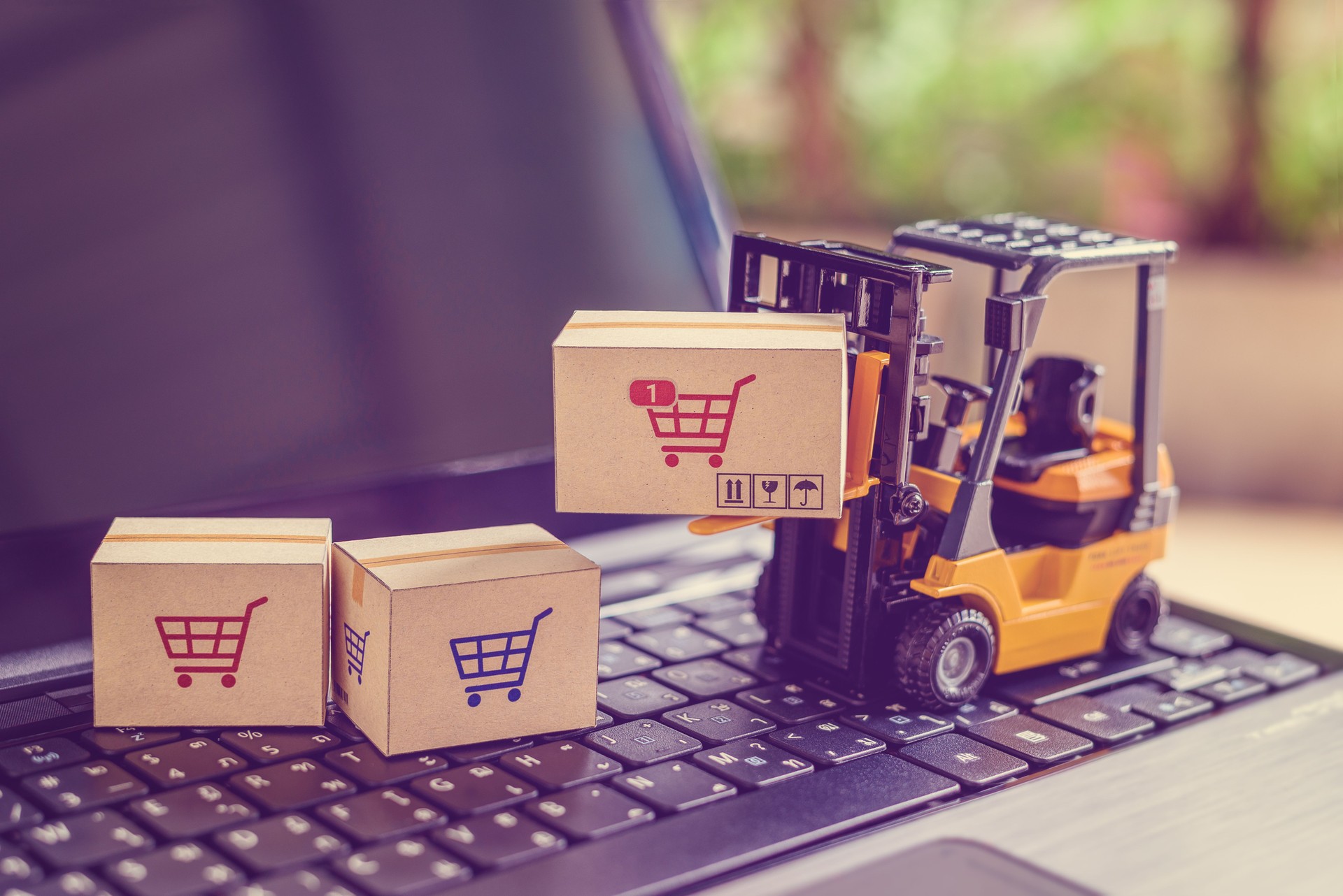 Logistics and supply chain management for online shopping concept : Fork-lift moves a box with a red shopping cart logo, 2 cartons on a laptop computer.
